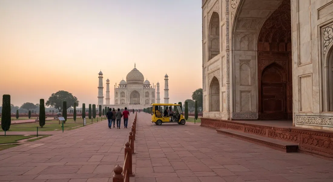 the East Gate approach to the Taj Mahal at dawn, with a quiet pedestrian path, a free electric buggy in the distance and the marble glowing faintly ahead