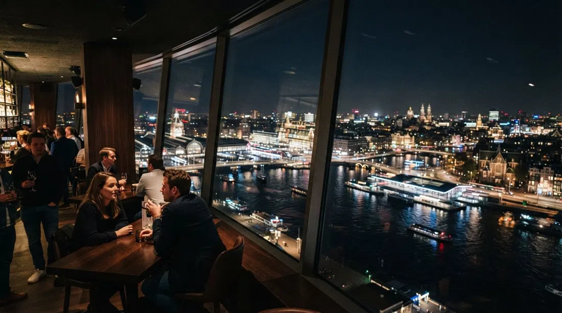 the 20th-floor Madam bar inside the A'DAM Tower at night, with panoramic IJ views and city lights spread below the windows