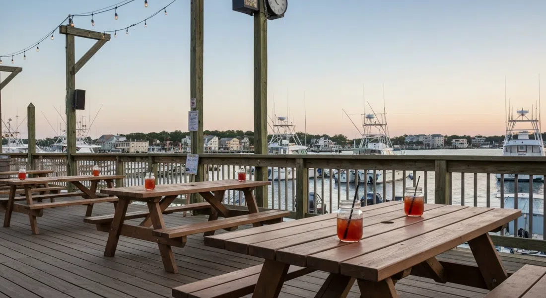 Back Bay Ale House deck at Gardner’s Basin in late-afternoon light, mason-jar cocktails on picnic tables with fishing boats and back-bay water beyond