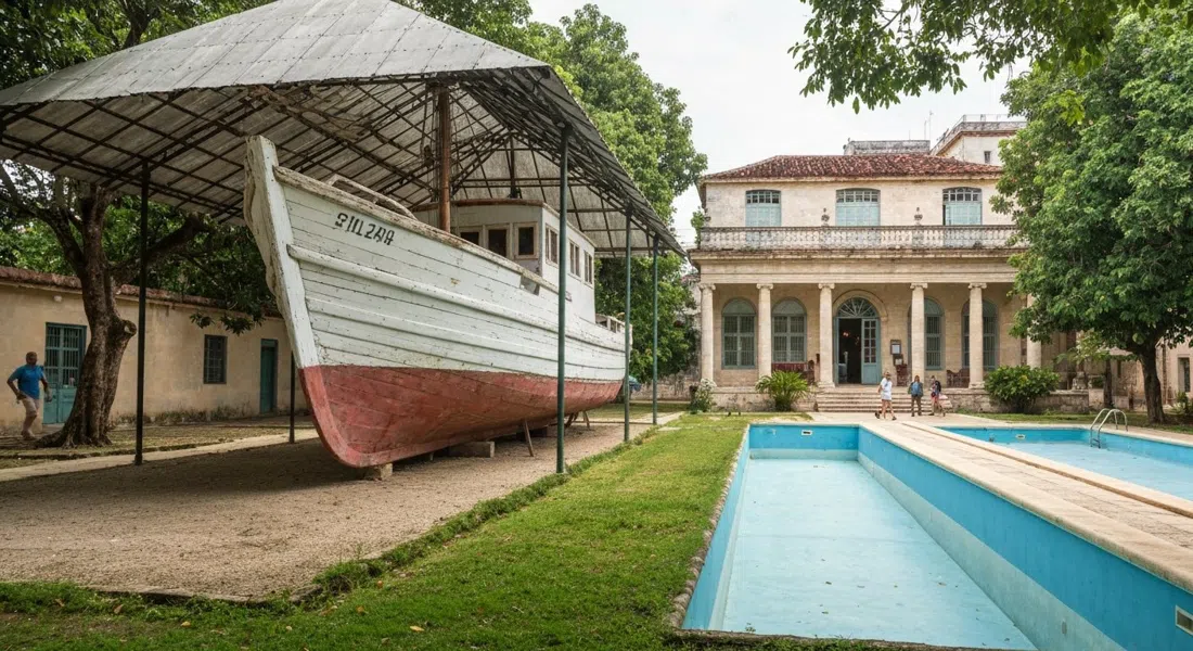 the restored Pilar under cover in the garden at Museo Hemingway Finca Vigía, with Hemingway’s house open behind and the empty pool nearby