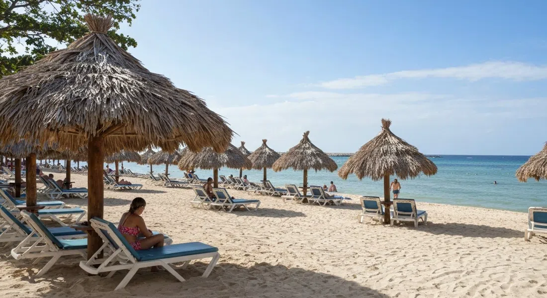 the private beach at Club Habana in Flores at midday, raked sand, palm-thatch umbrellas and the sea beyond the loungers