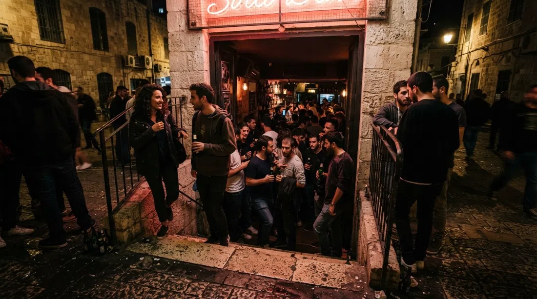 Sira bar on Ben Sira Street in Jerusalem, a narrow stairway descending into a dim cellar dive with neon glow, crowded doorway and late-night energy
