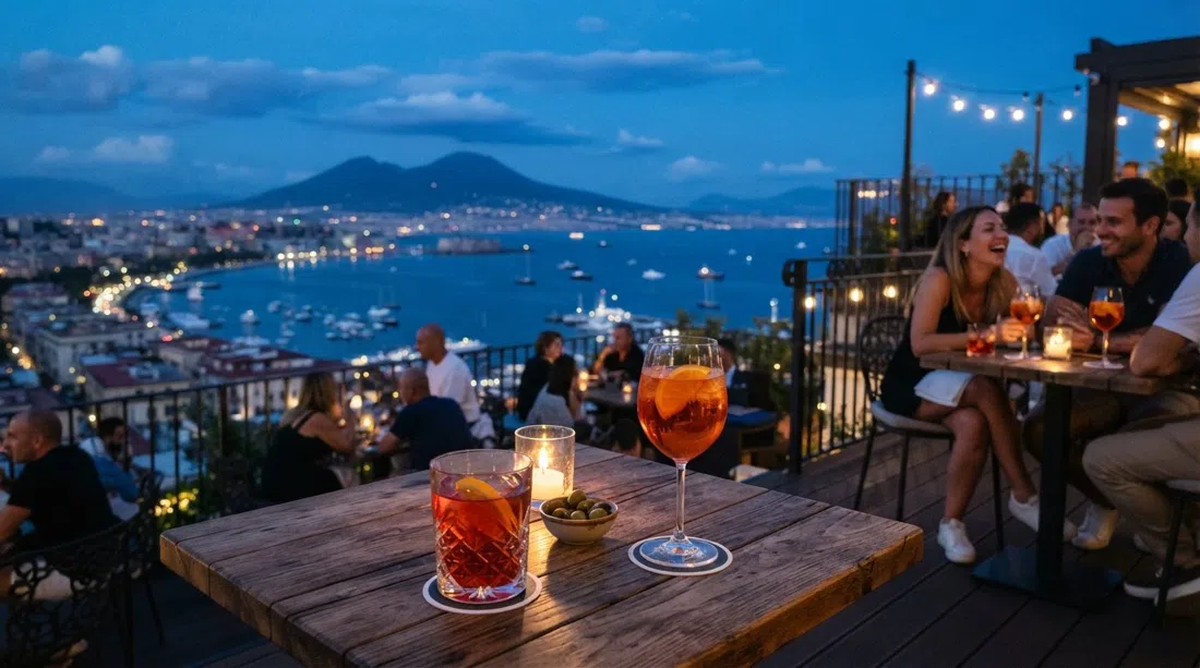 the terrace at Riserva Rooftop on Via Manzoni at blue hour, cocktail glasses in front of the city panorama and the bay beyond