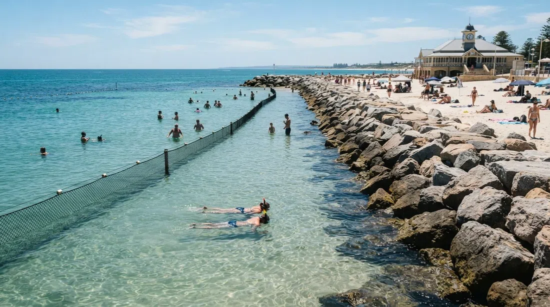 Cottesloe Beach in daylight, the granite groyne and calm sheltered water inside the seasonal shark barrier, with swimmers and snorkellers in the shallows