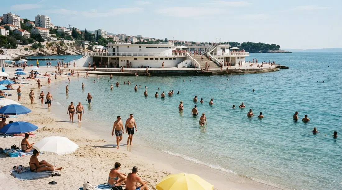 Bacvice beach in Split on a bright morning, shallow turquoise water over pale sand with swimmers wading far from shore and the beach pavilion behind them