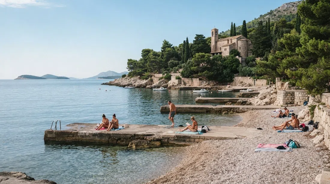 Ježinac beach below the Meštrović chapel, pebble cove with concrete platforms, pines and calm morning water