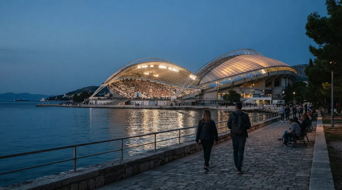 Stadion Poljud in Split at dusk, the shell-like roof glowing above the bay with the stadium bowl visible through the open structure