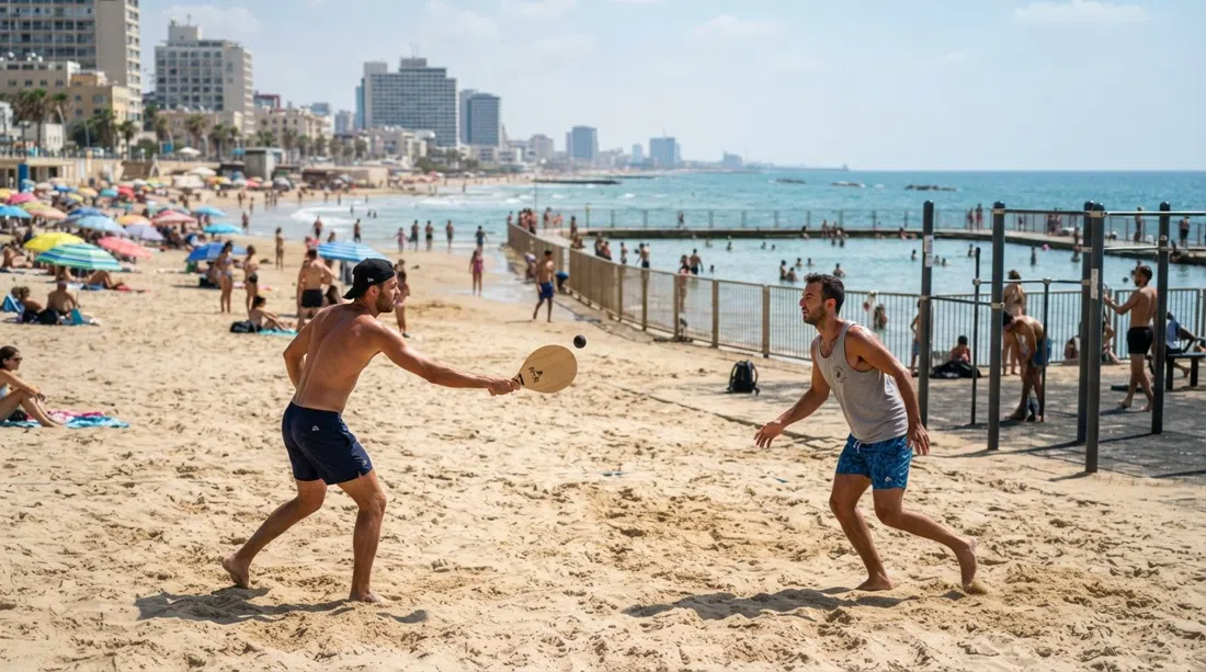 Gordon Beach in late-morning light, matkot players on the sand near the outdoor gym and the saltwater lido beside the water