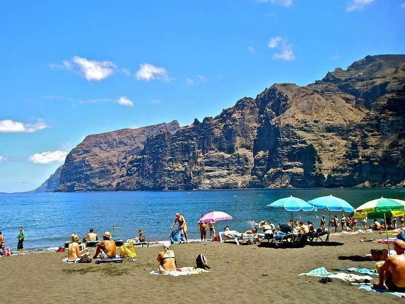 black volcanic sand and bathers at Playa de los Guíos beneath the cliffs