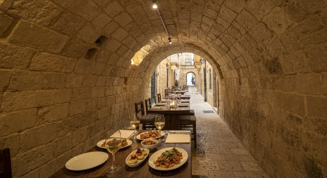 Legligin's candlelit stone cellar on Santa Lucia Street, small plates and local wine on a rustic table under vaulted stone