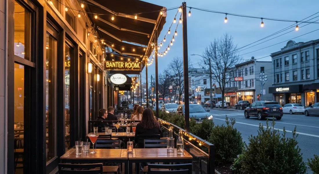 Banter Room on Mainland Street at dusk, a heated patio glowing under string lights with cocktail glasses and small plates on tables beside the sidewalk