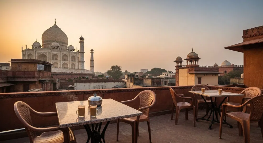 a rooftop terrace in Taj Ganj with the Taj Mahal dome visible beyond low roofs at sunrise, chai glasses and plastic chairs in the foreground