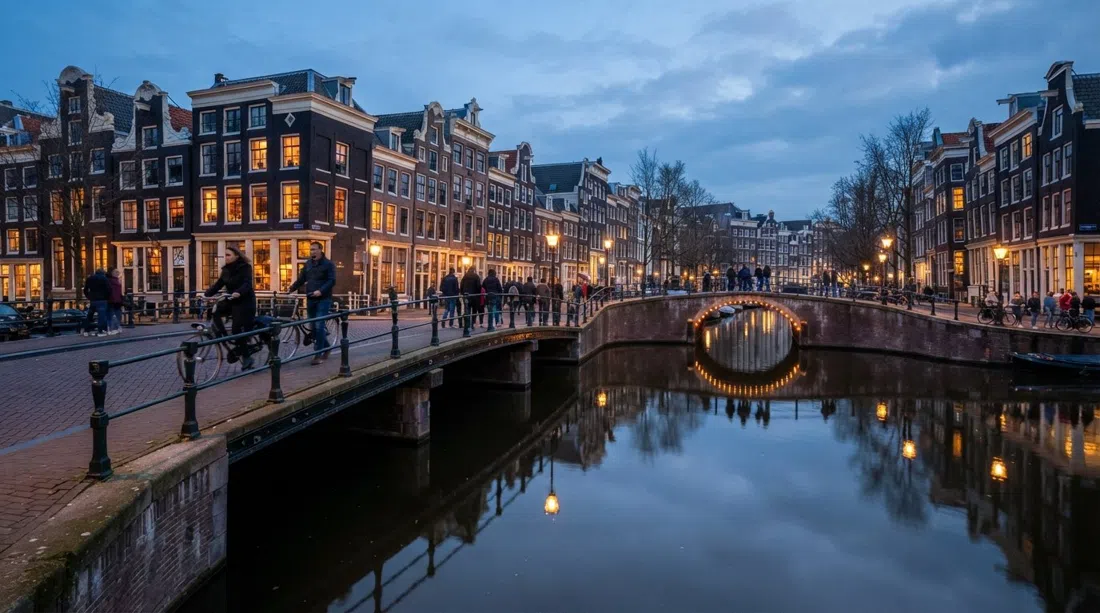 the Herengracht and its leaning 17th-century canal houses reflected in still water at dusk, a lit bridge in the foreground