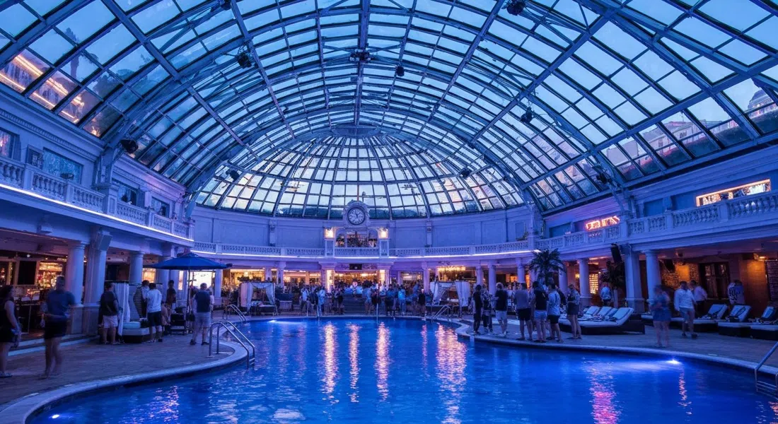 The Pool After Dark at Harrah’s, a glass-domed indoor pool nightclub with blue lighting, cabanas and a DJ crowd after dark
