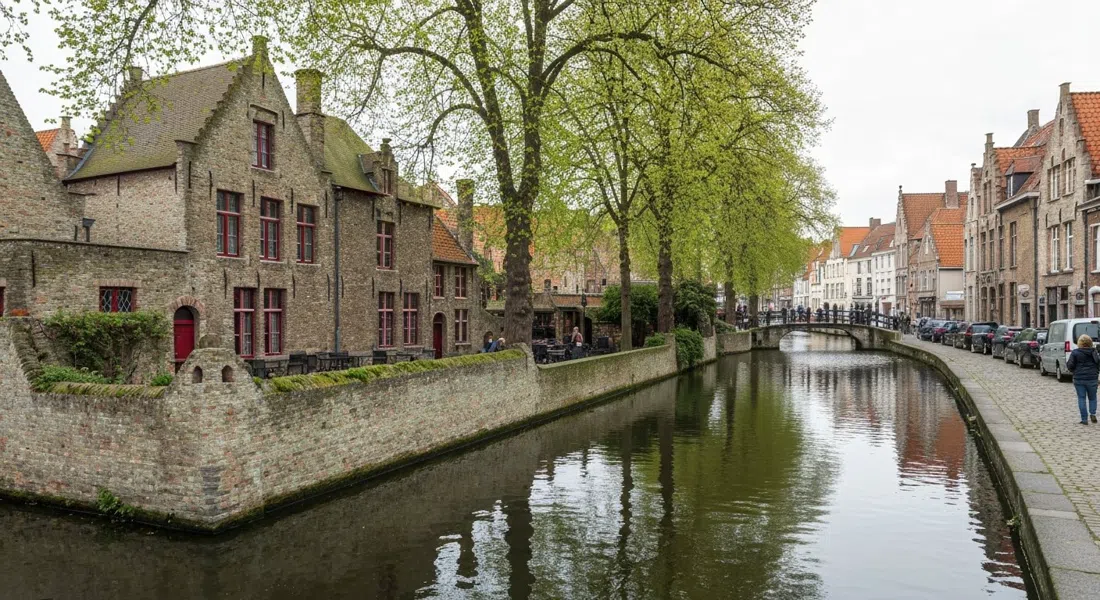 the Langerei canal beside Sint-Gillis, tree-lined water with no boats, gabled houses reflected in the surface and a narrow cobbled path running along the bank