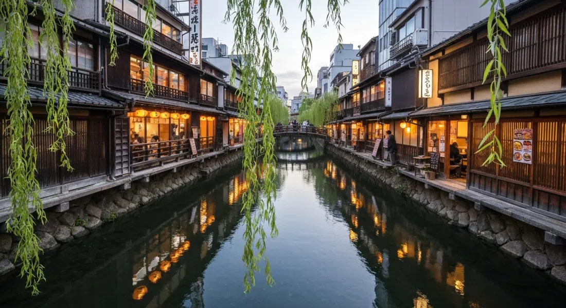 The Shirakawa canal in Shinbashi at dusk, willow branches over the water and wooden restaurant facades reflected below
