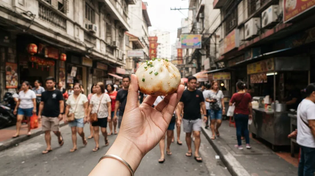 Shanghai Fried Siopao on Ongpin Street, a crisp-bottomed pork-and-chive bun being held up close on a busy Chinatown pavement at midday