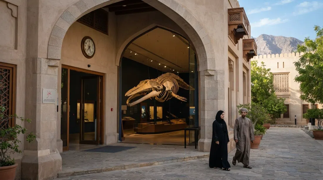 the Natural History Museum of Oman entrance in the Ministry of Heritage complex, with the mounted sperm-whale skeleton visible inside a compact, quietly lit gallery